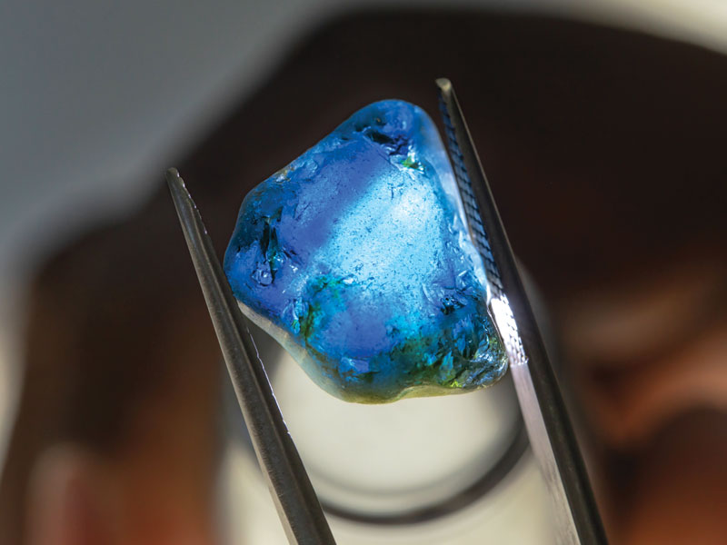 uncut color gemstone held by tweezers