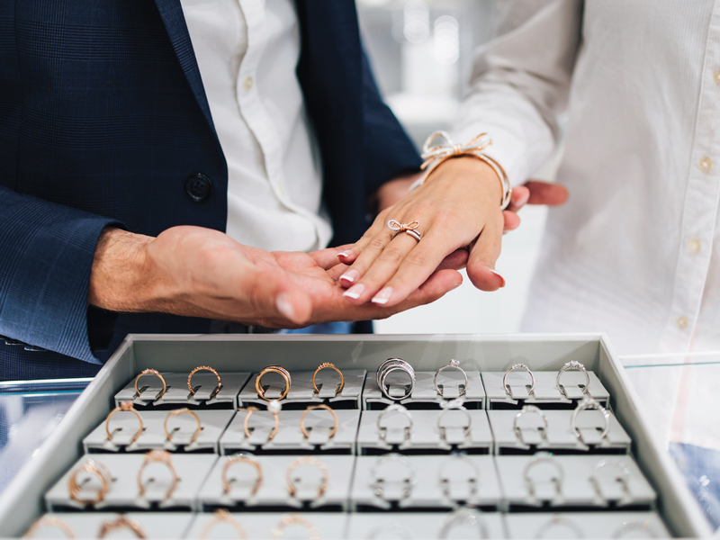 Couple in front of jewelry display tray trying on rings.